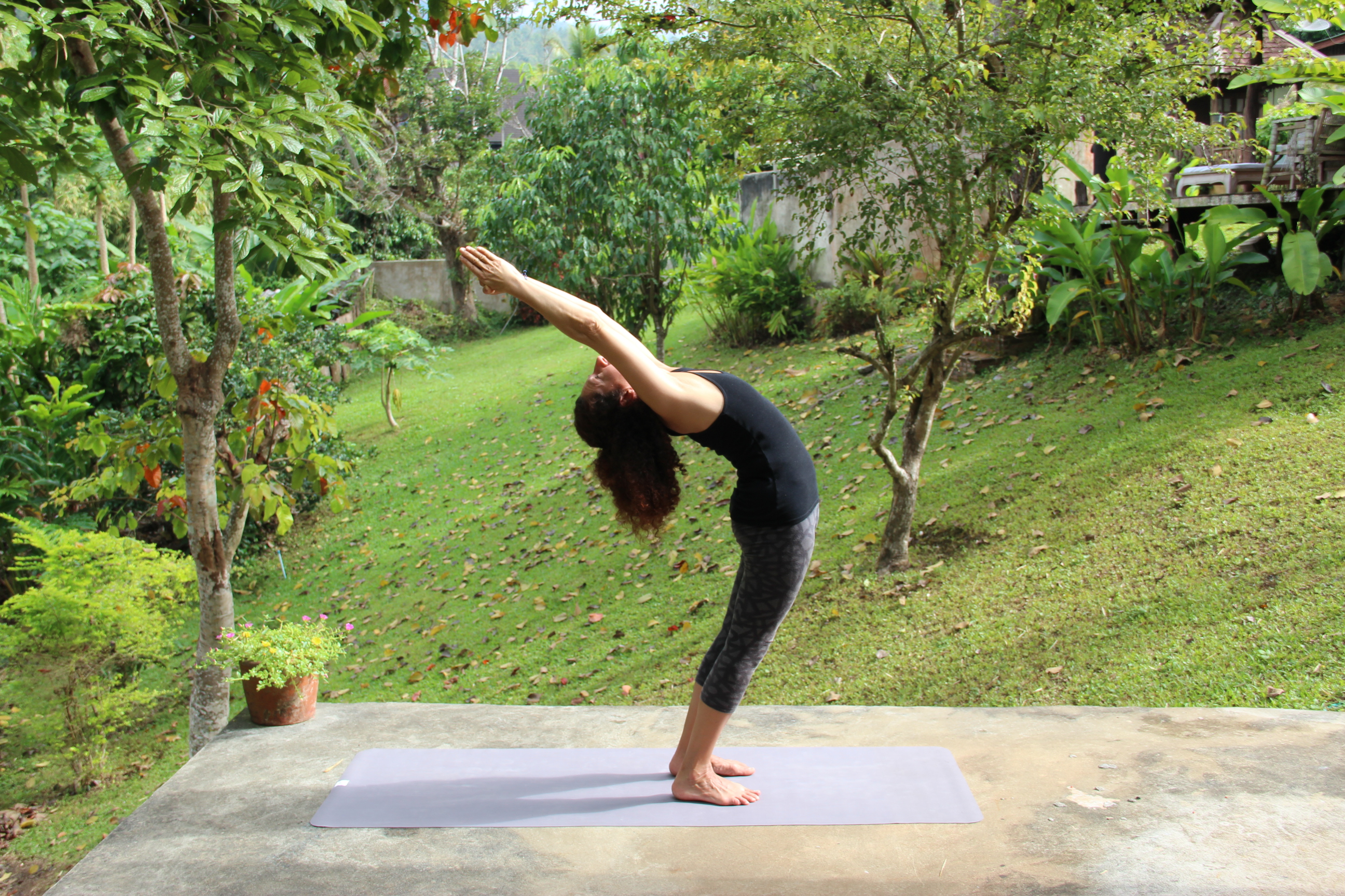 A person practicing yoga outdoors, performing a backbend on a yoga mat in a lush green garden.